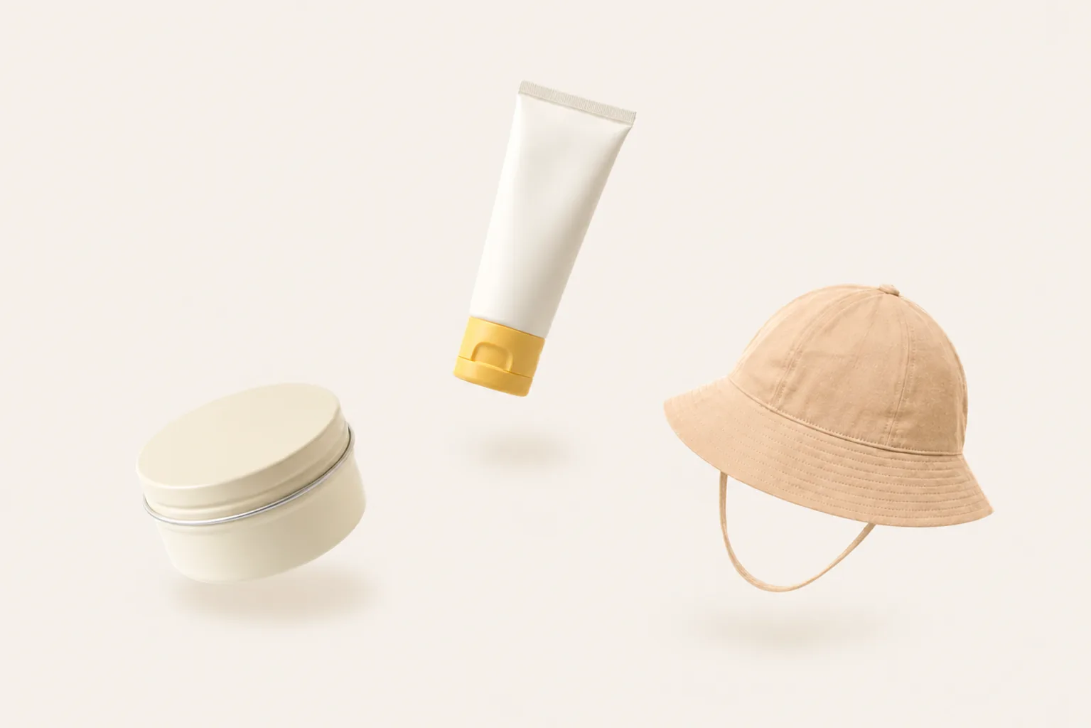 Wind cream, mineral sunscreen and a wide-brim baby sun hat arranged on an ivory studio ground