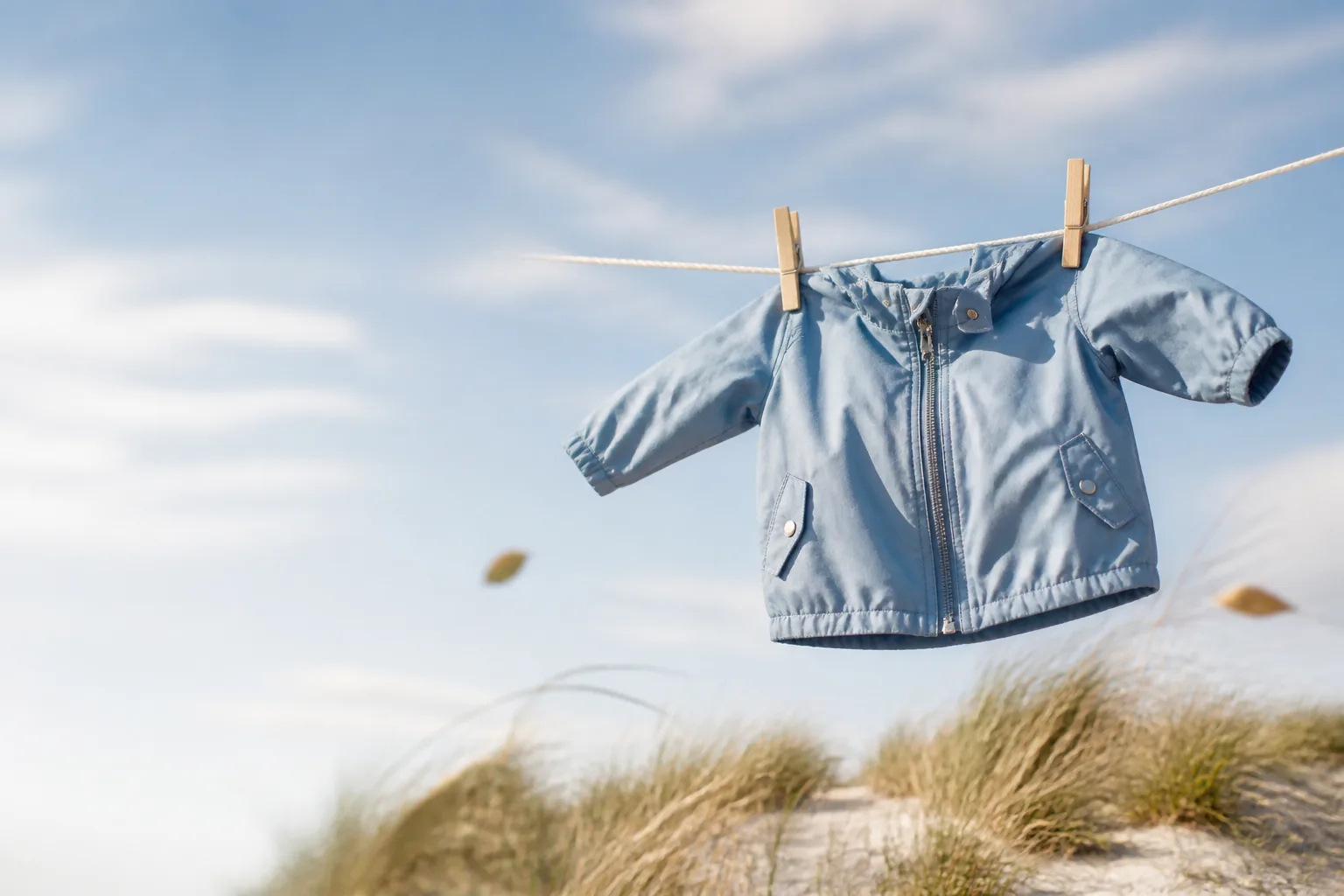 A soft blue baby jacket caught by the wind on a clothesline